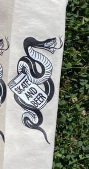 Camiseta Actus de la serie Skate and Beer en color beg y logotipo de serpiente con lata de bebida. Disponible en The Gallery Surf Shop, tienda de surf y skate en Málaga.